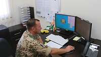 Ein Soldat sitzt in einem Büro vor zwei Computerbildschirmen