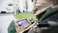 Over-the-shoulder shot: Using a monitor and a control unit, a soldier steers the small drone flying in front of him.