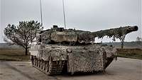 A tank with camouflage netting is parked on a concrete surface.