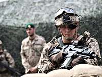 A soldier with the digital “Future Infantryman” system and a G36k rifle stands in front of a camouflage net.