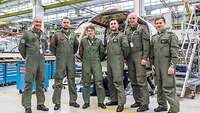 Six soldiers in flight suits stand in front of a fuselage of the new helicopter model on the shop floor.