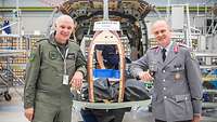 Two soldiers stand in front of the unfinished fuselage of an LUH SAR aircraft.