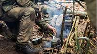A soldier prepares food on a small fire.