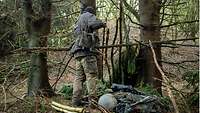 A soldier uses branches to build a shelter in the forest.