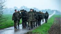 A group of soldiers carry tree trunks on their shoulders during a march.