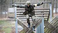 A soldier jumps over an obstacle of wooden beams