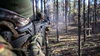 A soldier fires a weapon into the forest.