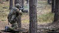 A soldier fires his weapon in the forest