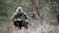 A soldier crouches in a clearing, holding his weapon in the collapsed low ready position.