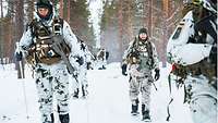 Six soldiers in snow camouflage move in column using snowshoes – small, oblong platforms strapped to their feet. 