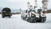 A Hägglunds oversnow vehicle is parked next to a heavy truck on snowy ground. 