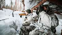 Two soldiers crouch in a covered position dug out of the snow. One of them observes the surroundings 