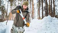 A soldier digs a trench in the snow. Snow is piled up behind her. 