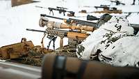 A sniper in snow camouflage lies prone in the snow with his rifle at the ready. 