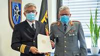 Prof. Hecken und Generalstabsarzt Dr. Schoeps stehen mit Mund-Nasen-Maske in Uniform nebeneinander. Hecken hält seine Urkunde.