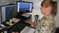 Eine Soldatin sitzt am Schreibtisch und hat zwei PC Monitore vor sich