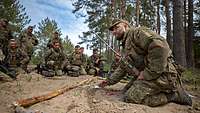 Soldaten hocken im Wald um einen Ausbilder herum. Er erklärt etwas.