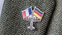 Ein Anstecker mit einem Flugzeug und einer französischen und deutschen Flagge.
