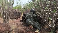 Hinter einem Stein liegend und von Sträuchern umgeben beobachtet ein malischer Soldat das Gelände