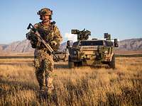 Ein Soldat vor einem Panzerspähwagen Fennek in wüstenartiger Landschaft