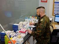 Ein Mann mit einem Stift in der Hand und Papier vor ihm hält in der linken Hand eine Arzneimittelpackung
