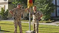 Zwei Soldaten stehen gemeinsam an einem Flaggenmast
