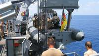 Das Speedboot mit Besatzung hängt am Kran auf Höhe der Reeling. Davor stehen zwei Soldaten und unterstützen