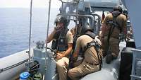 Die Besatzung sitzt im Speedboot. Der Steuermann hält ein Funkgerät vor dem Mund und prüft die Verbindung