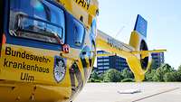 ADAC Hubschrauber mit der Aufschrift Bunswehrkrankenhaus Ulm, dahinter das Gebäude des Krankenhaues