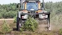 Ein Mann fährt in einem Traktor mit Mulch-Anhänger auf einem Truppenübungsplatz.