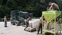 Mehrere Soldaten befüllen mit einer Füllmaschine Sandsäcke. Ein Radlader der Bundeswehr steht zur Abholung bereit.