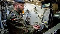 Ein Soldat sitzt im Kampfpanzer an einem Computerbildschirm und schreibt auf einer Tastatur.