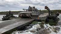Eine Schwimmschnellbrücke hat das Ufer erreicht, ein Panzer rollt über einen Metallsteg an Land.