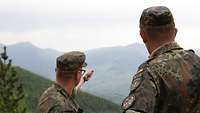 Zwei Soldaten stehen nebeneinander. Einer von ihnen deutet mit der Hand auf das Gelände im Hintergrund