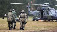 Vier Soldaten mit einer Rettungstrage laufen auf einen wartenden Hubschrauber zu.