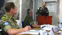 Ein Soldat steht an einem Redepult. Im Vordergrund sitzt Boris M. mit einem weiteren Soldaten an einem Tisch 