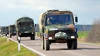 Lastkraftwagen der Bundeswehr fahren auf einer Straße hinter einander.