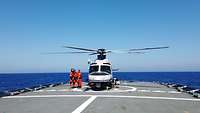 Ein Hubschrauber steht auf einer Landeplattform an Bord eines Schiffes. Drei Personen steigen aus dem Hubschrauber aus.
